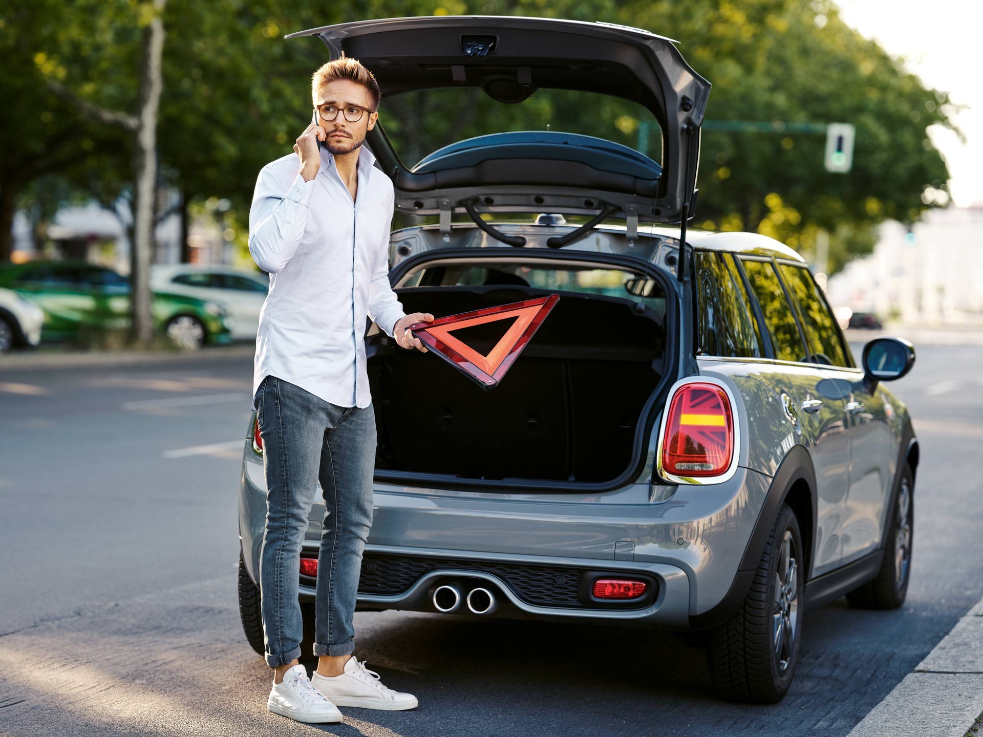 Driver placing a warning triangle beside a MINI in White Silver Metallic with the tailgate open.